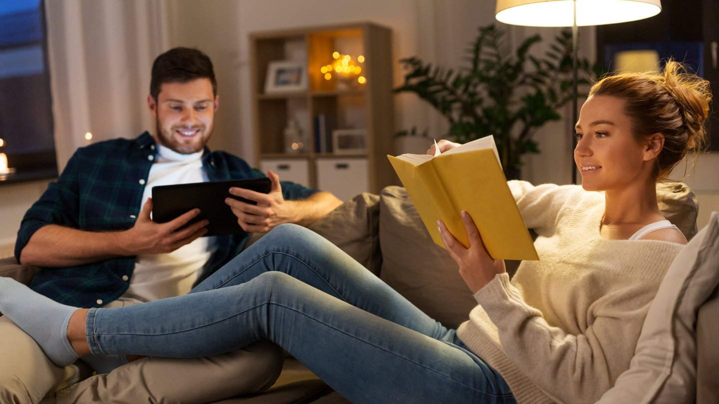 Junger Mann und junge Frau sitze am Sofa und lesen unter Stehlampe